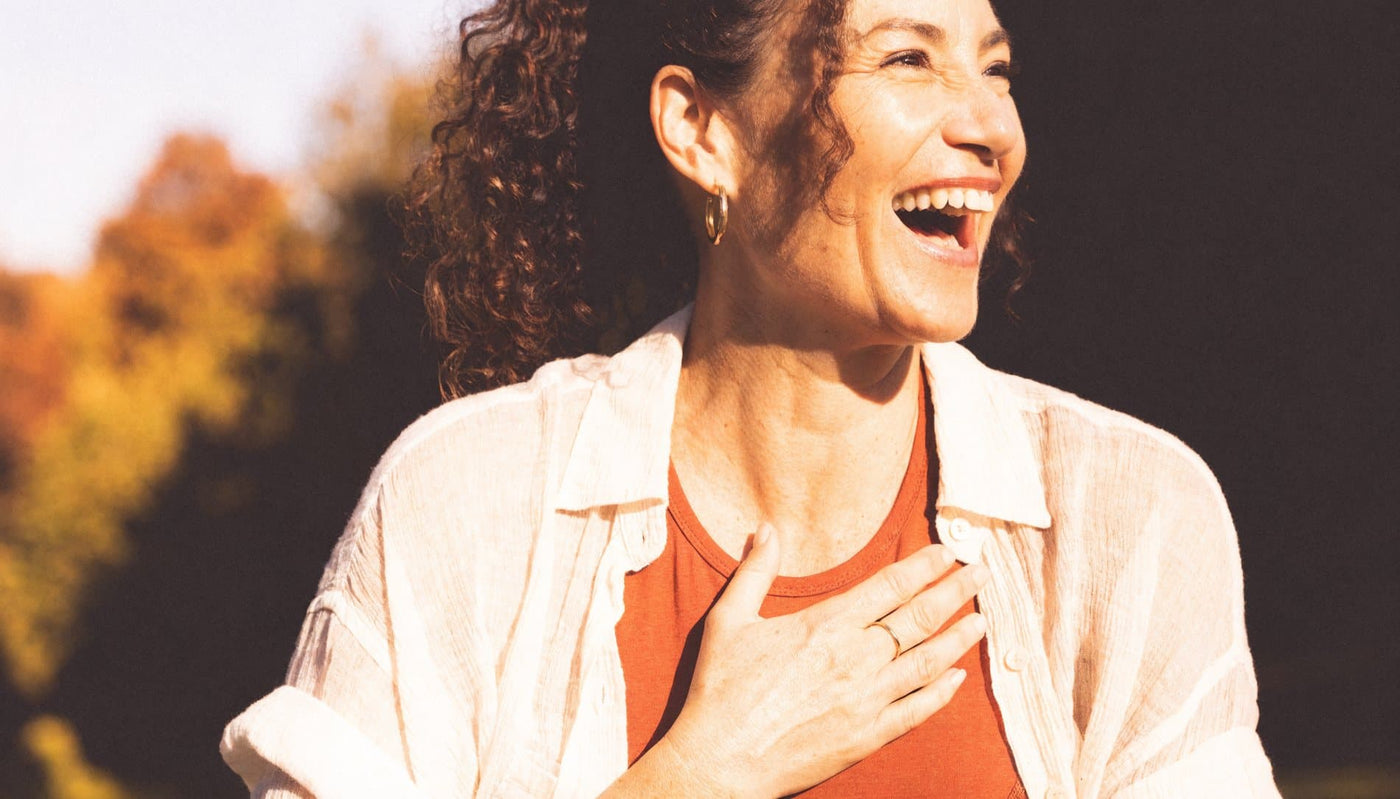 A woman laughing in autumn sunlight, one hand resting on her chest