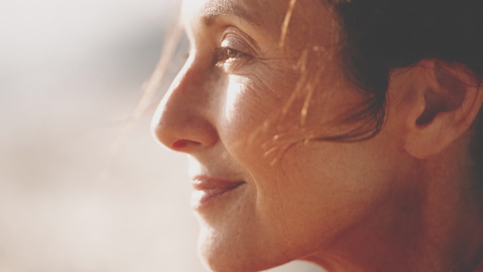 A woman in a rust-coloured coat turning toward bright daylight, relaxed and unhurried, in gentle motion